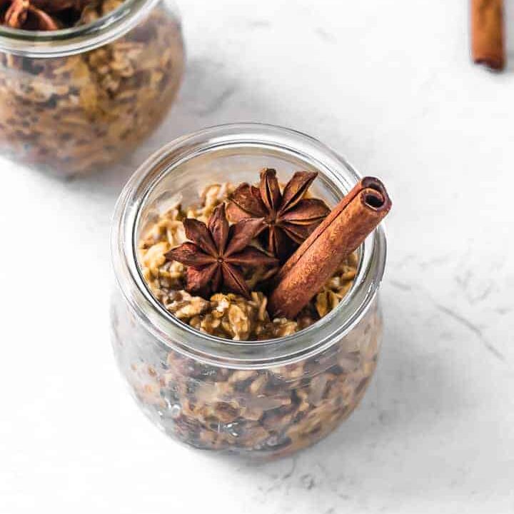 A glass jar filled with overnight oats with a cinnamon stick and star anise on top