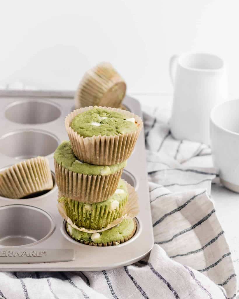 Gluten free white chocolate matcha muffins stacked in a muffin tin on a striped napkin