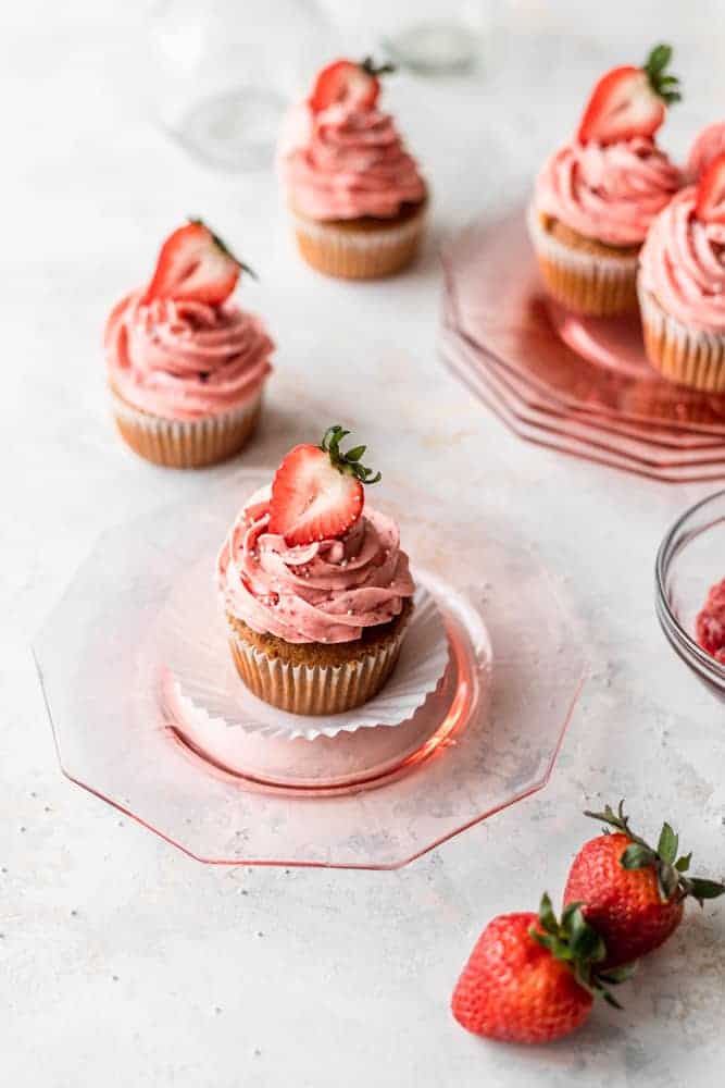 cupcakes topped with pink frosting and fresh strawberries on depression glass plates