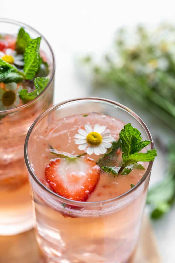 A pink cocktail in a glass garnished with a strawberry slice and mint.