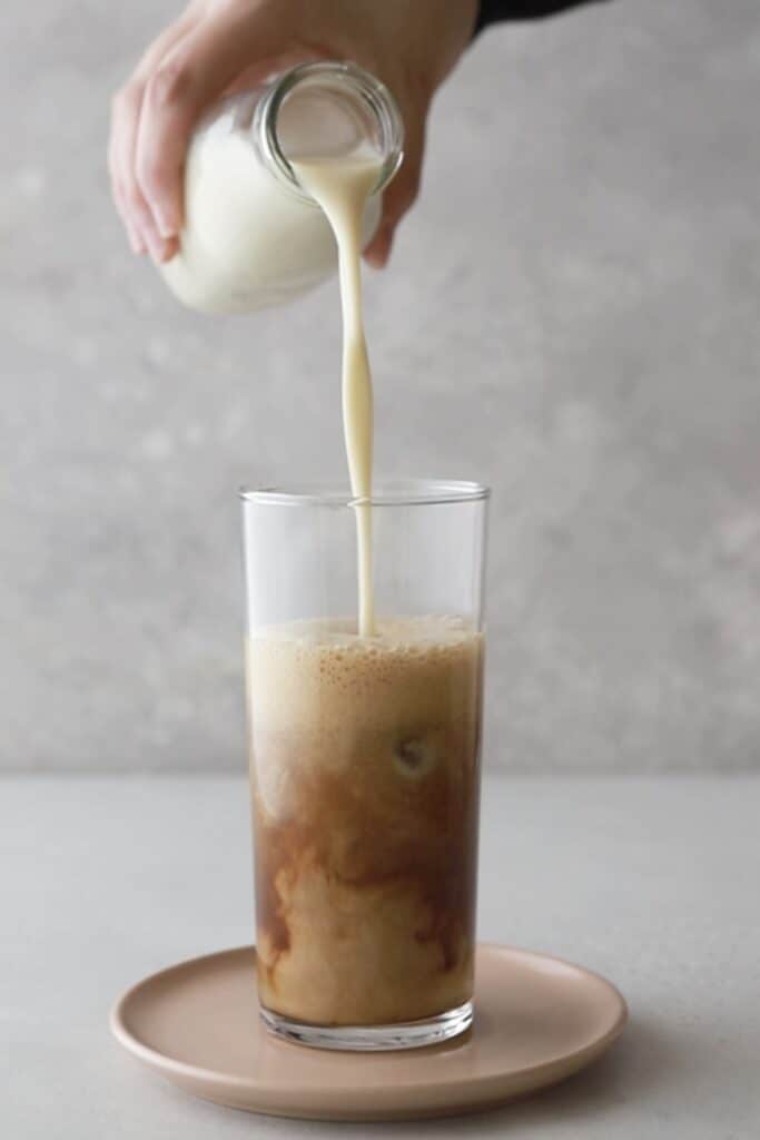 Pouring oat milk into a glass with espresso.