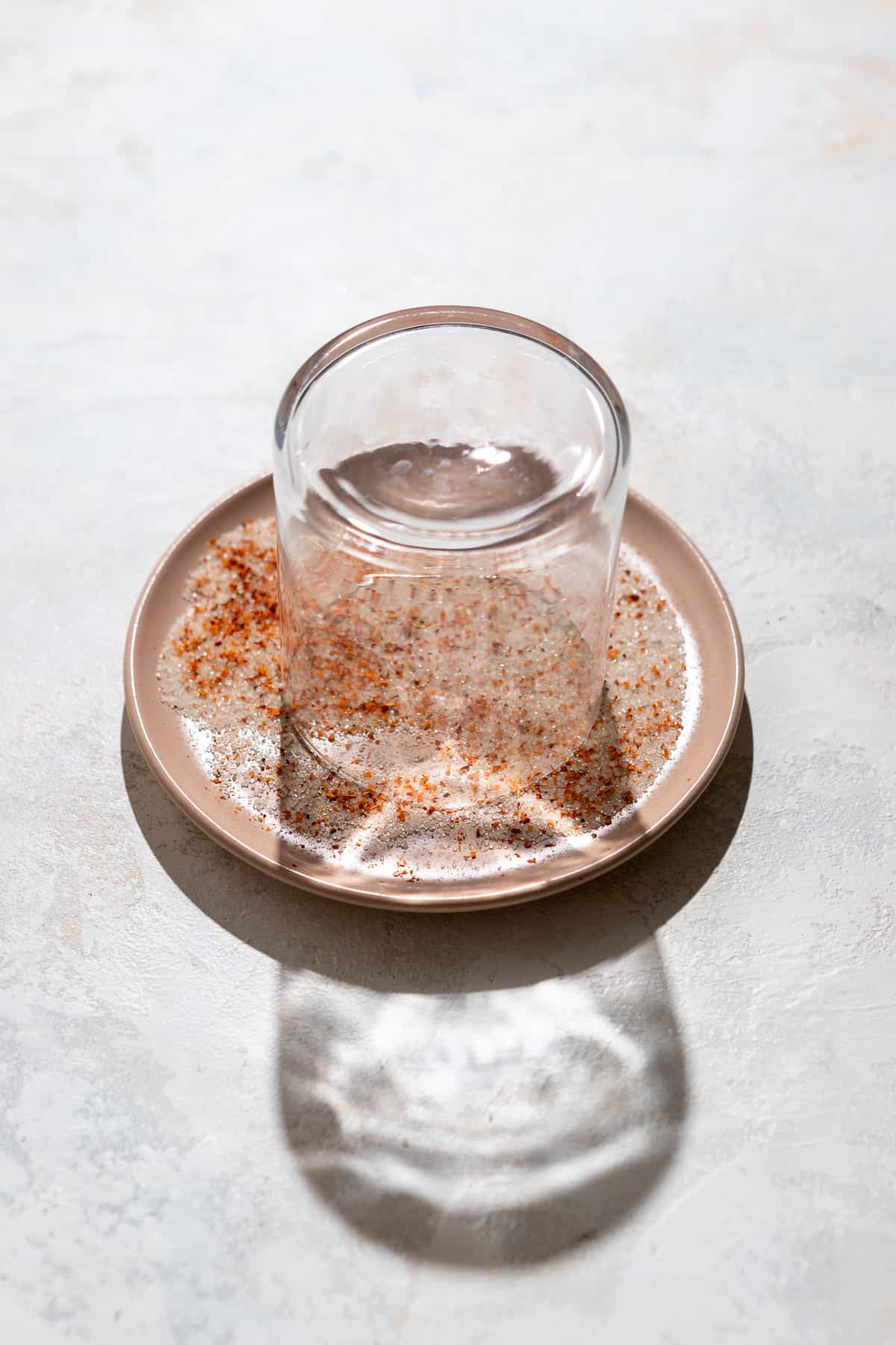 A glass upside down on a plate with sugar and Tajin seasoning.
