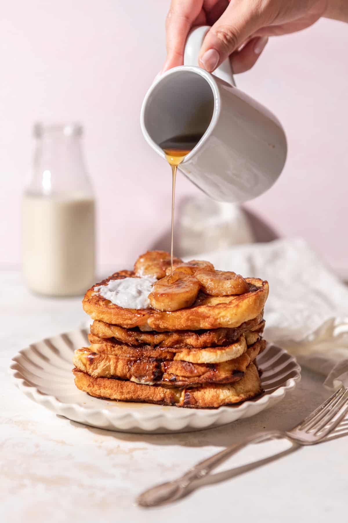 Maple syrup being poured over a stack of French toast on a plate.