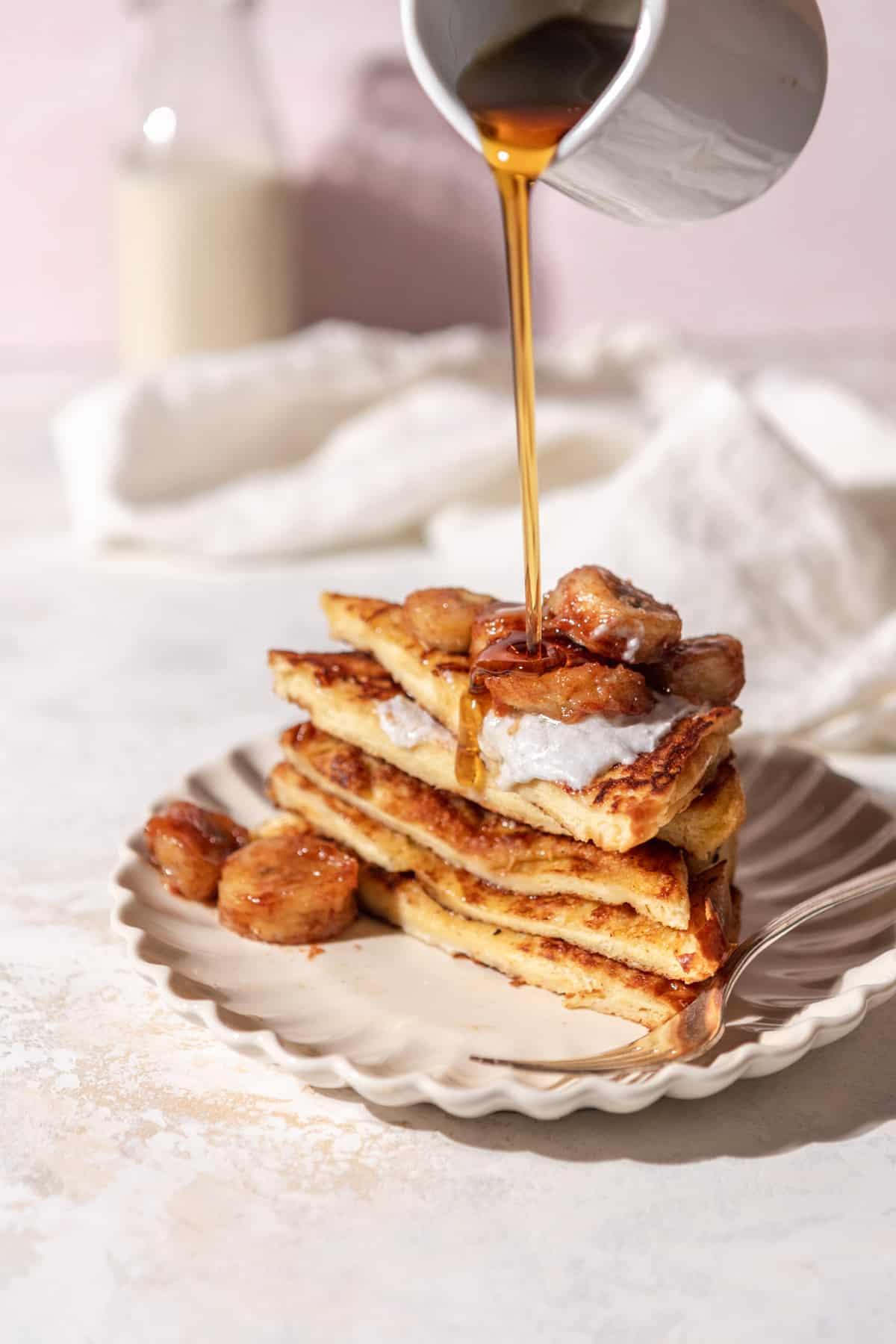A stack of sliced French toast with maple syrup being poured over it.