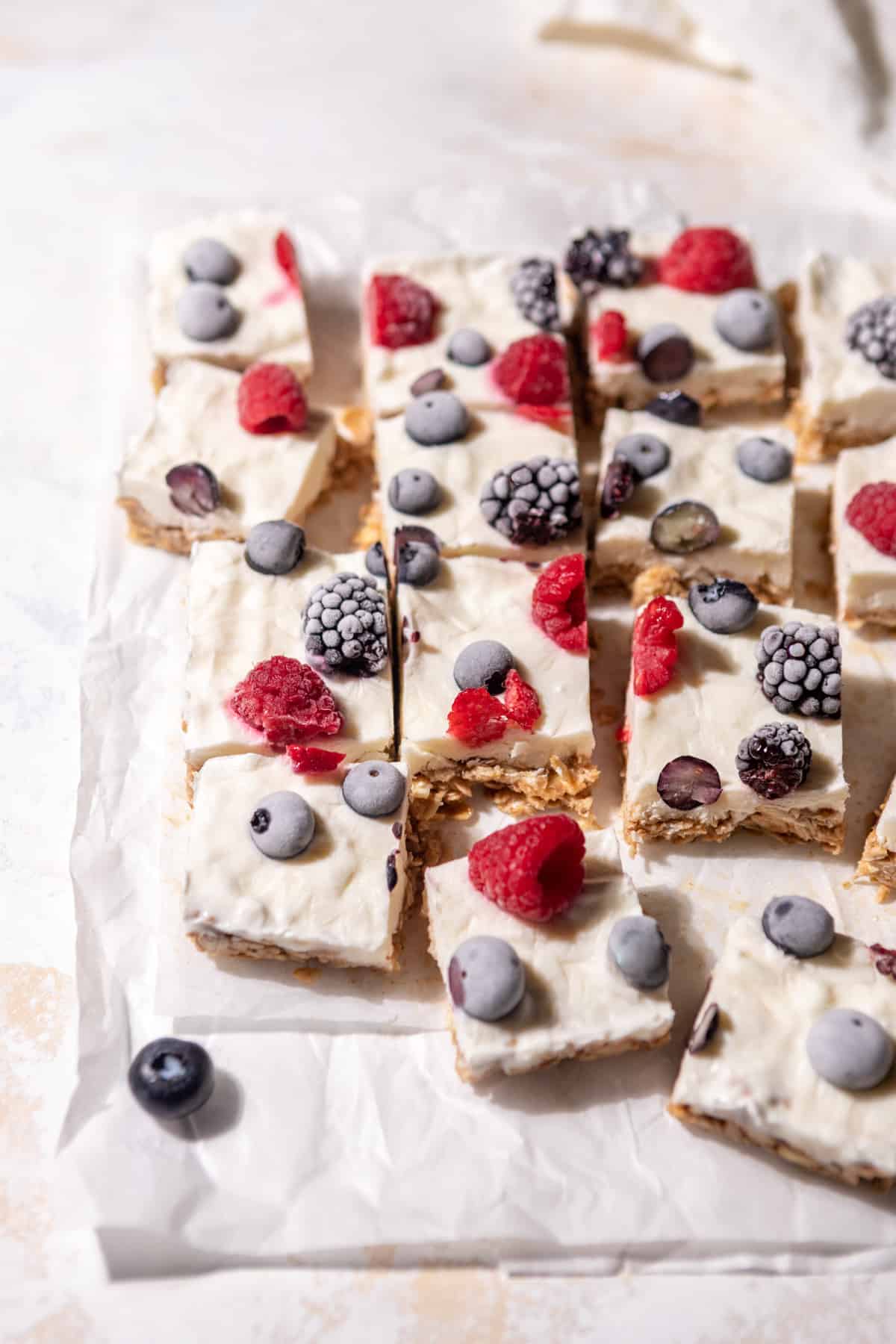 Frozen yogurt bar squares on parchment paper topped with a variety of fresh berries.