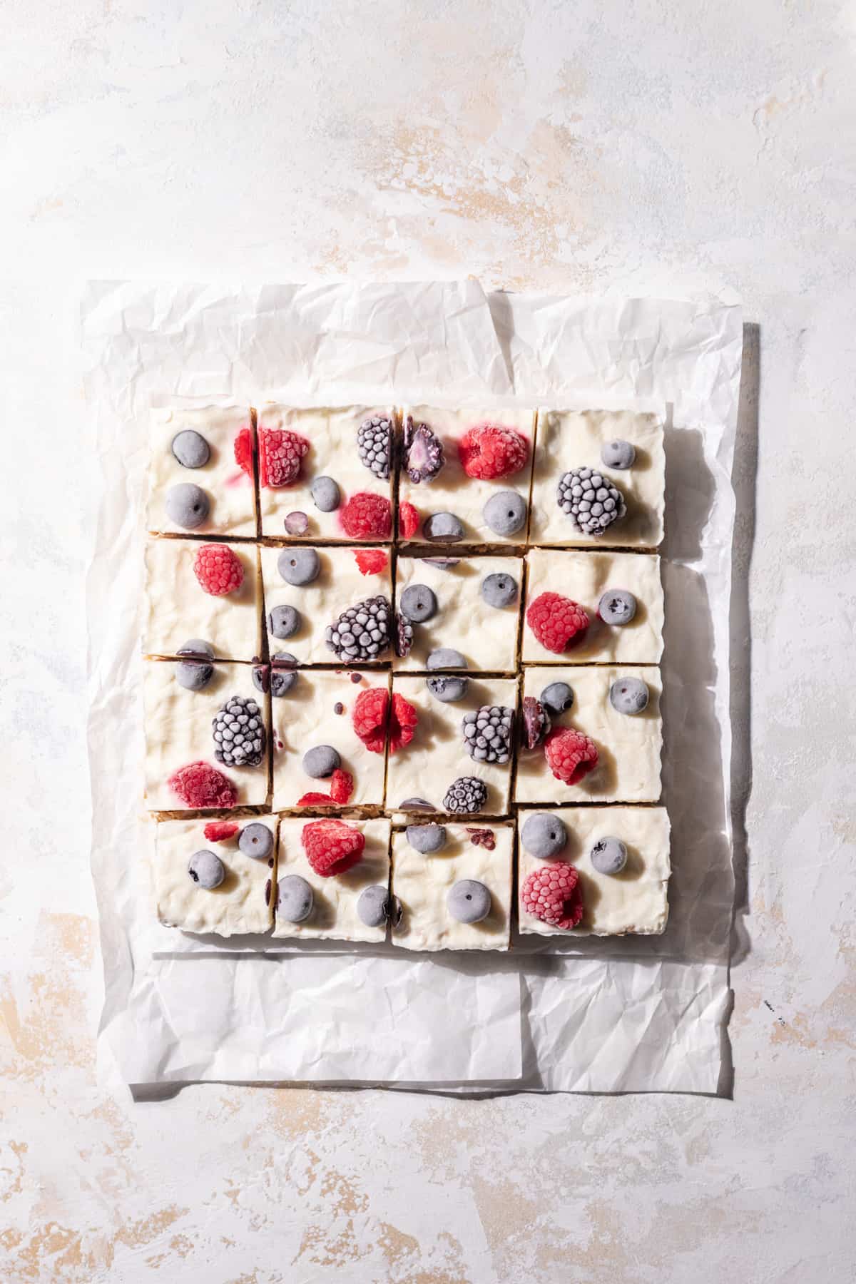 Frozen greek yogurt granola bars sliced on parchment paper topped with a variety of berries.