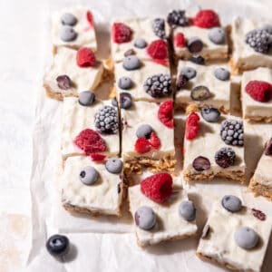 Square frozen greek yogurt granola bars topped with berries on parchment paper.