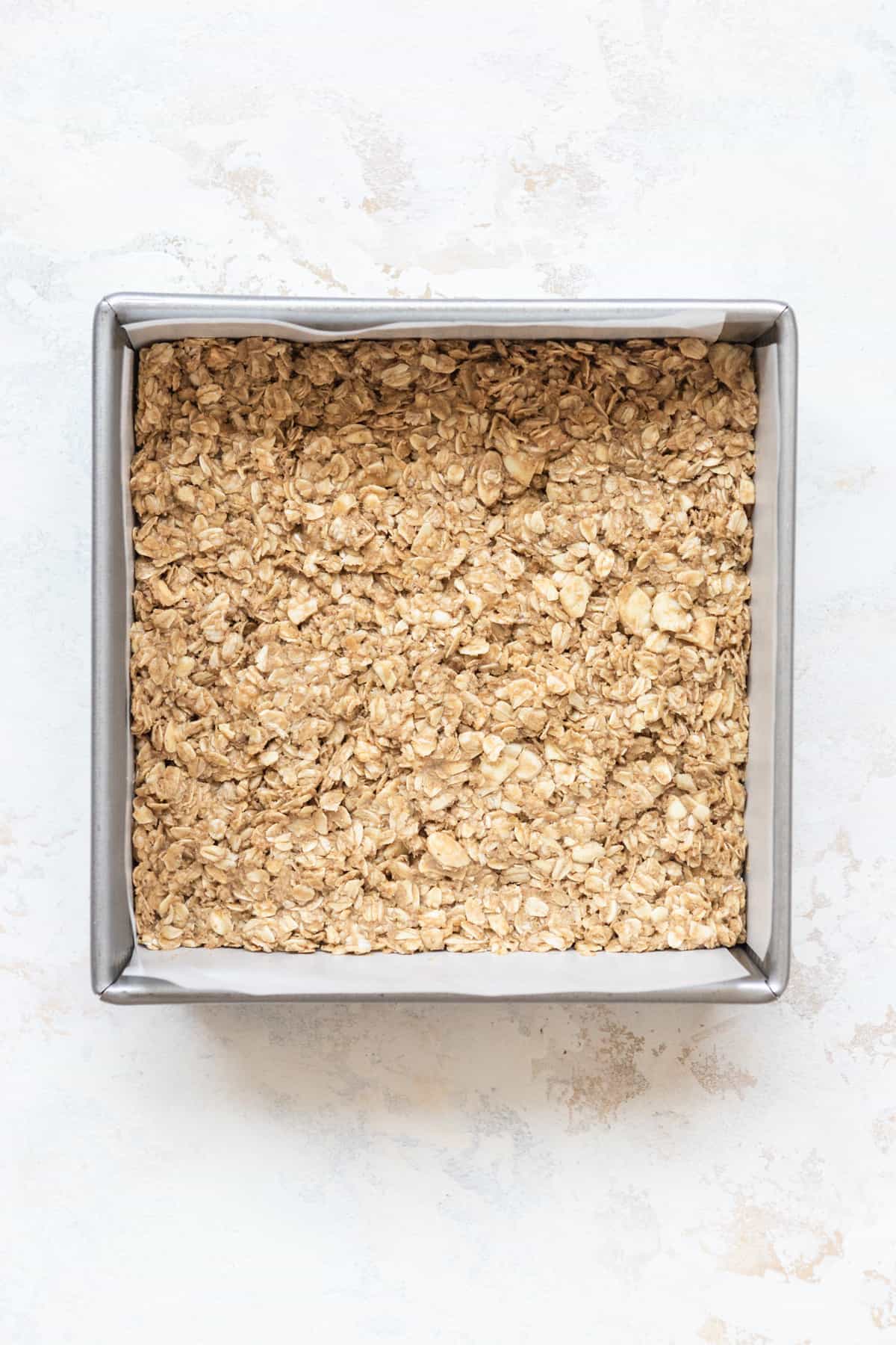 Granola base pressed down in a square baking pan.