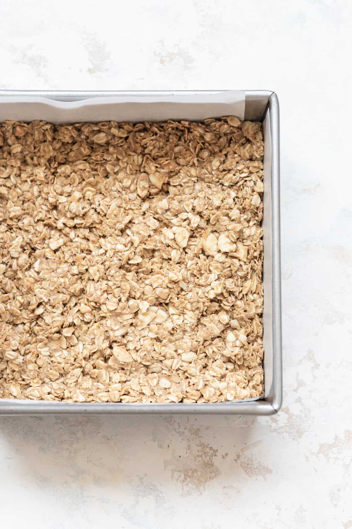 Granola base pressed down in a lined square baking pan.