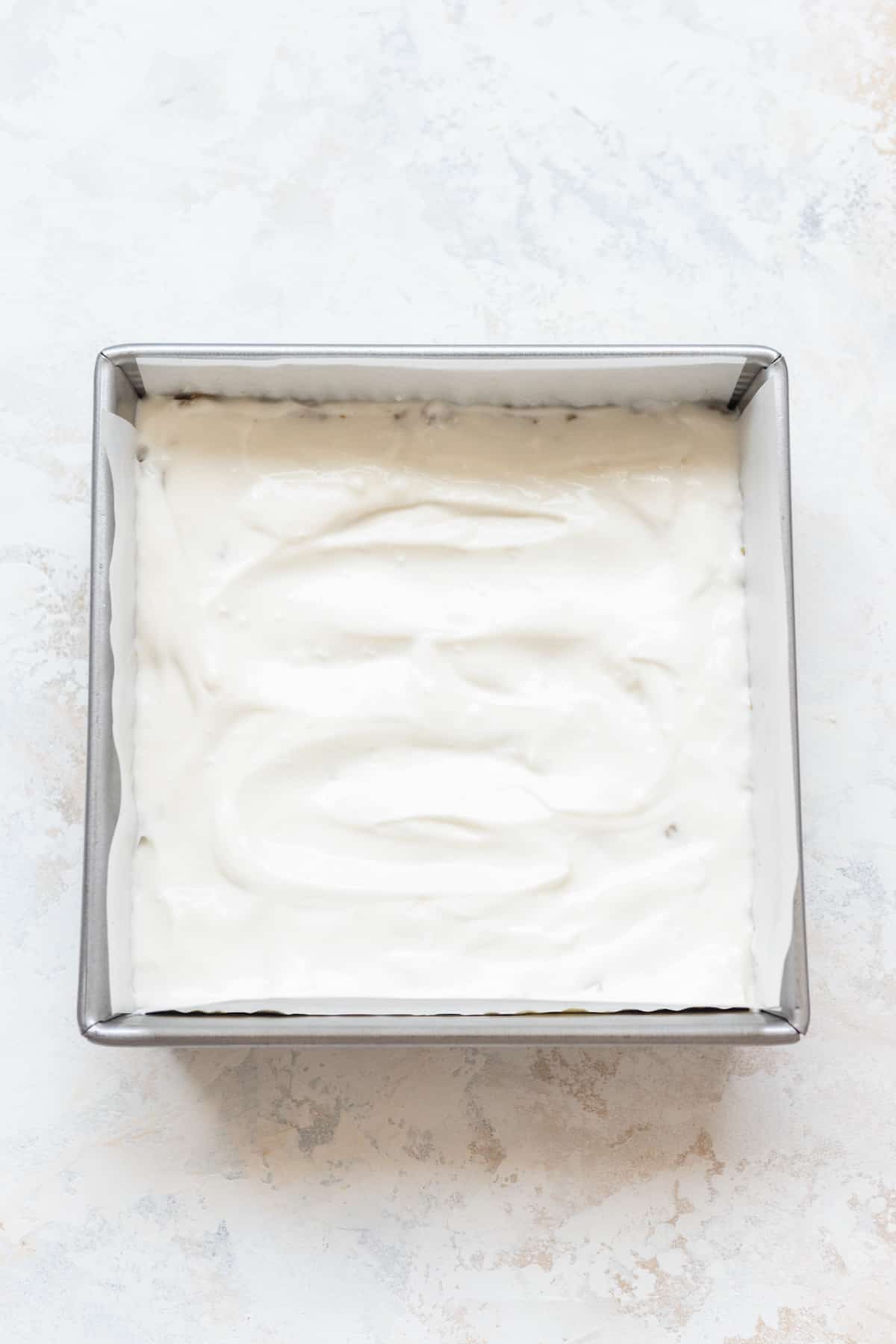 Greek yogurt on top of granola in a square pan.