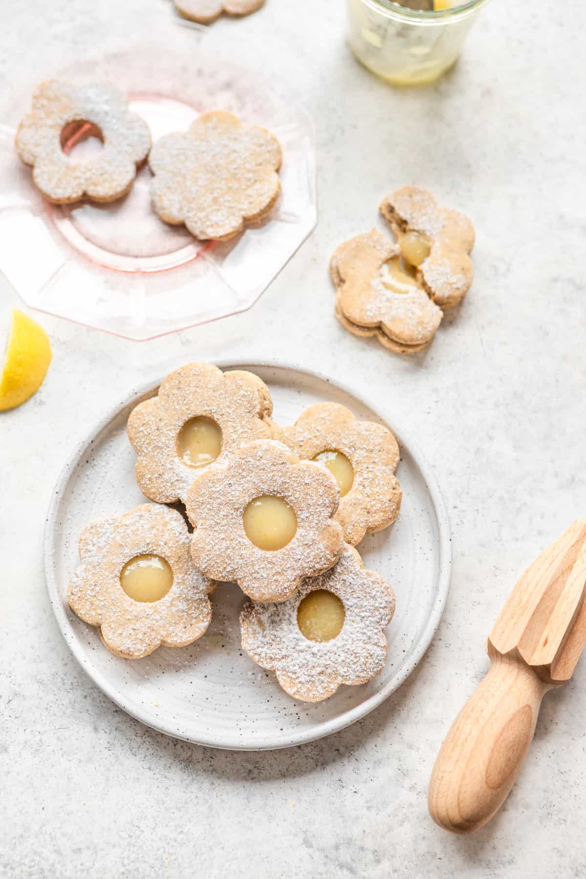Flower shaped vegan shortbread cookies filled with lemon curd on white and pink plates.
