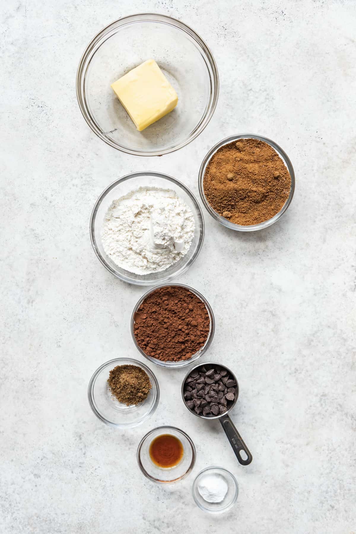 Ingredients to make eggless double chocolate chip cookies on a white surface.