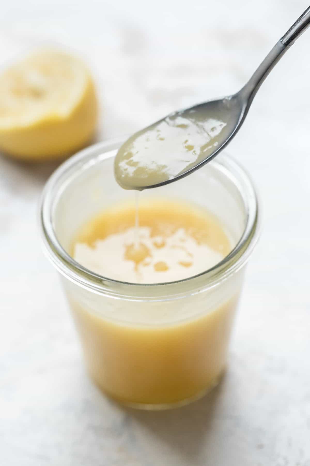 Lemon curd dripping off a spoon into a jar.