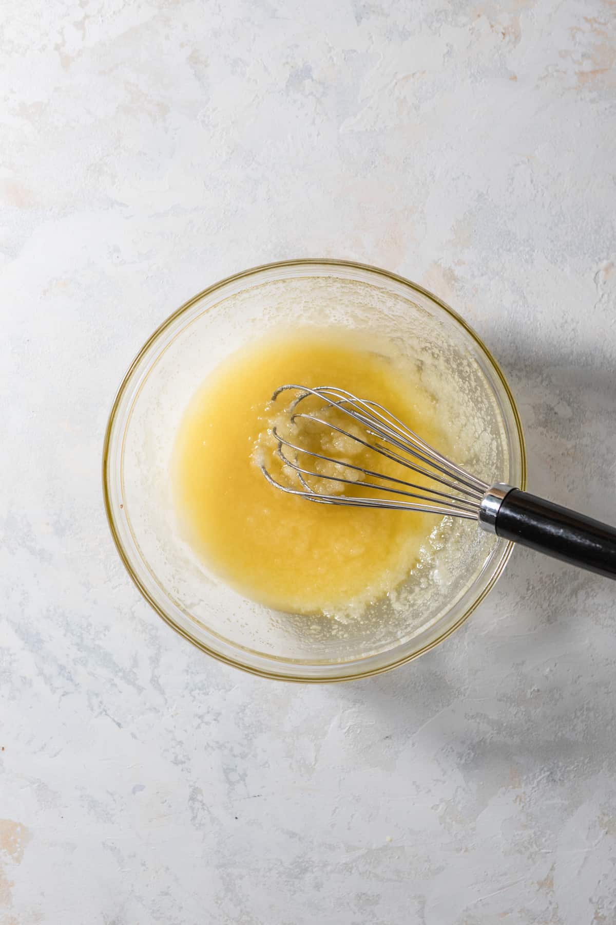 Melted butter and sugar whisked together in a glass bowl.