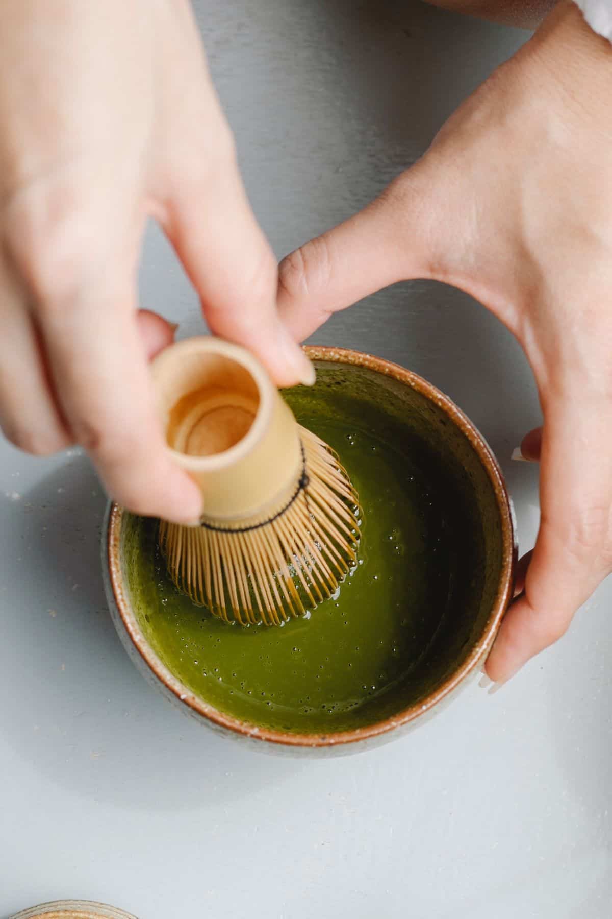 A person making matcha in a bowl with a bamboo whisk.