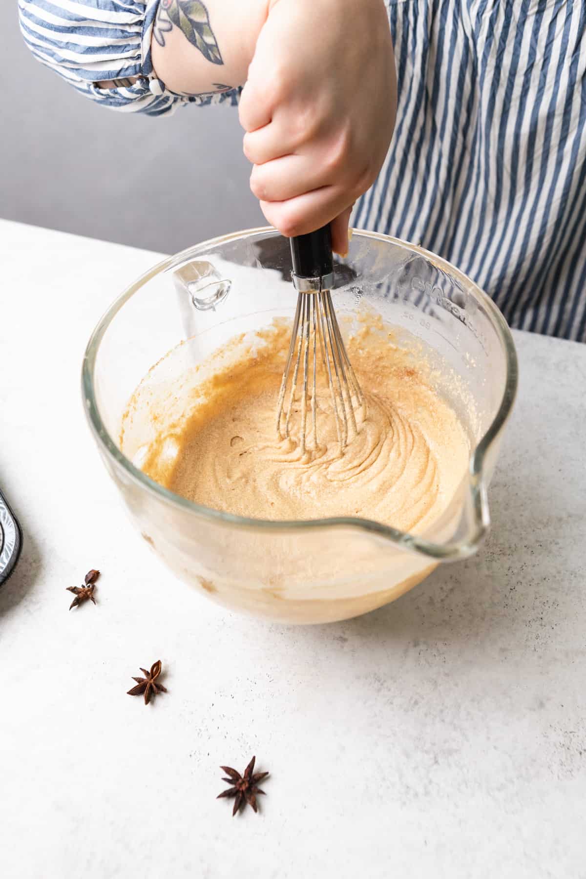 A person mixing cupcake batter with a whisk in a large glass bowl.