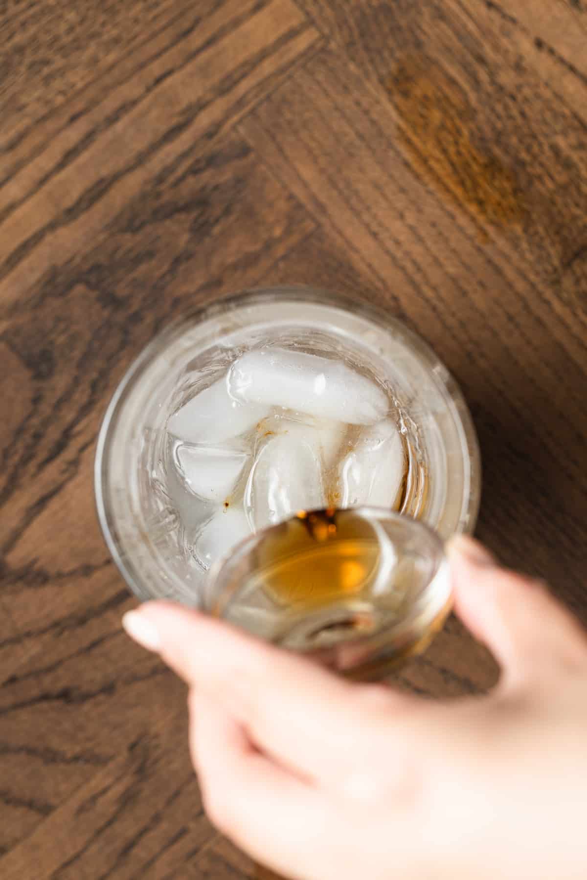 Pouring maple syrup into a cocktail shaker filled with ice.