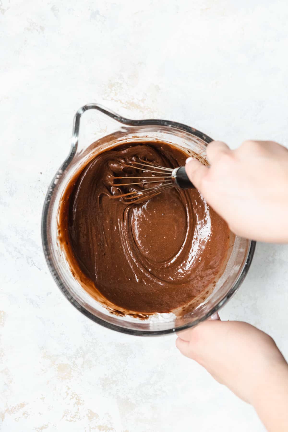 Chocolate cake batter being whisked in a clear bowl.