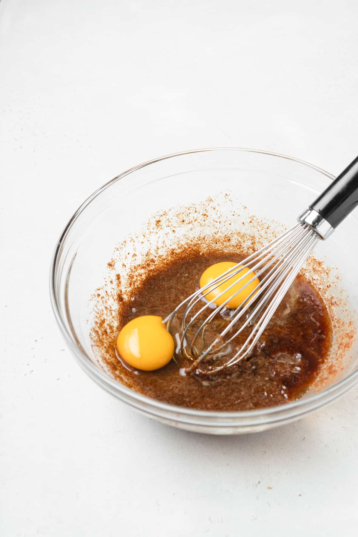 Eggs in a bowl of coconut sugar and butter with a whisk.