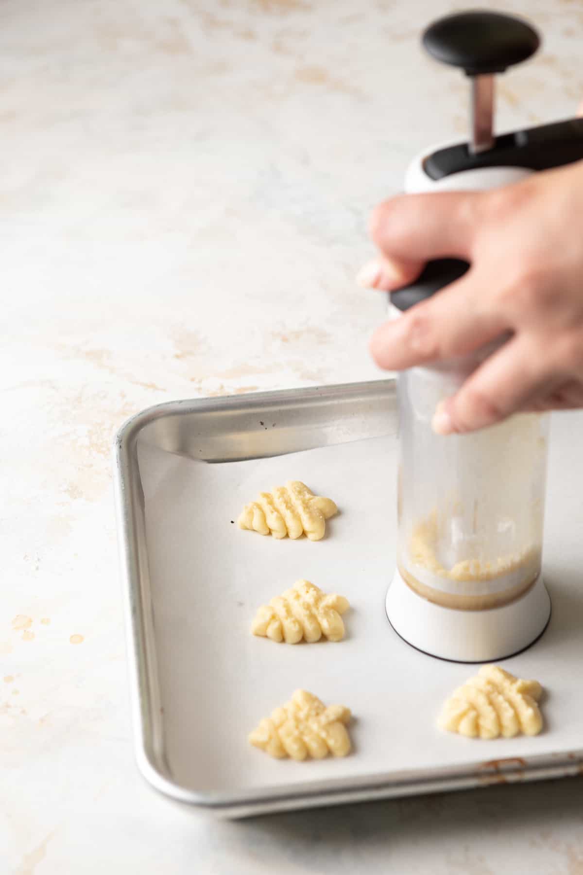 Pressing Christmas tree shaped cookie dough on a baking sheet with a cookie press.