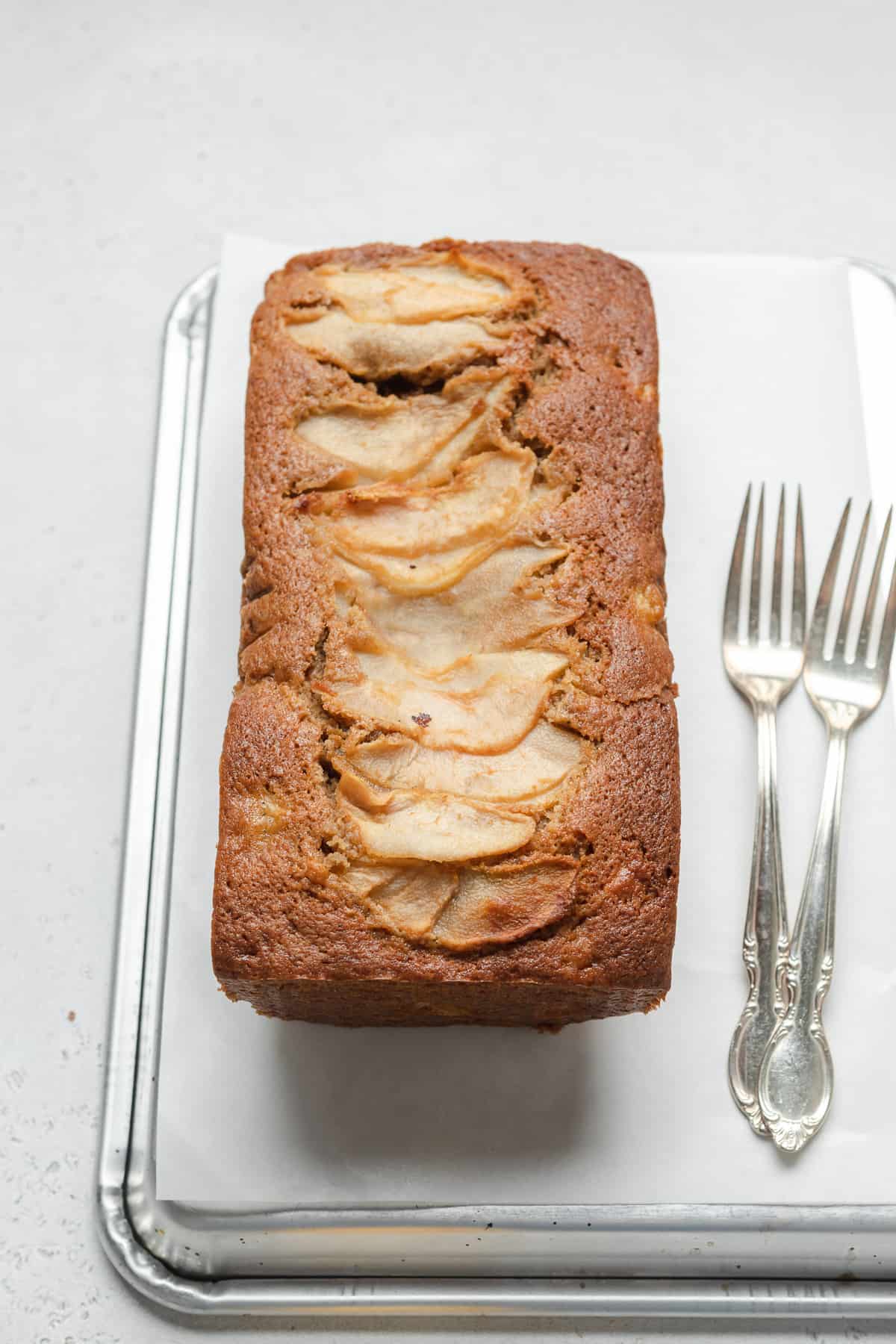 ¾ view of pear bread with sliced pears on top next to 2 forks.