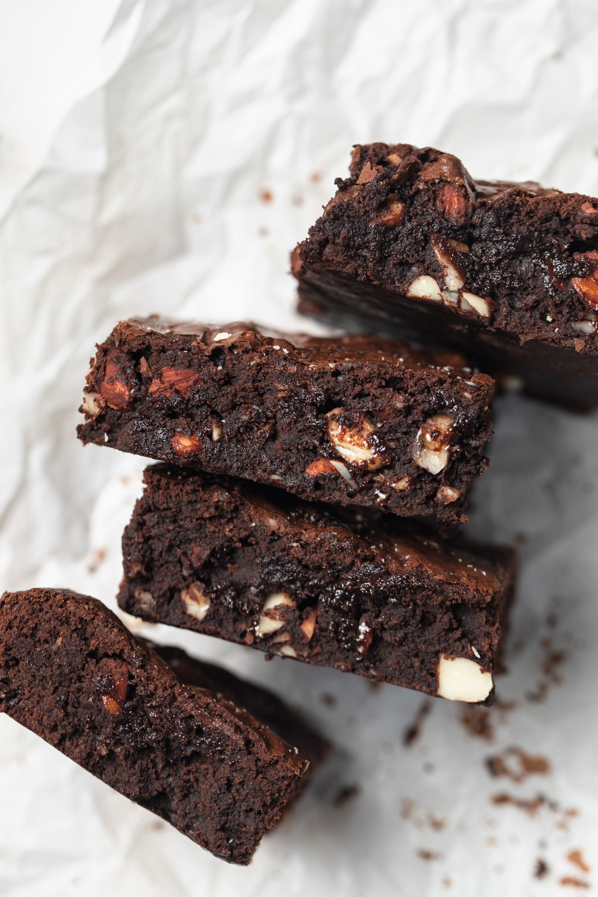 Brownies with nuts stacked on parchment paper.