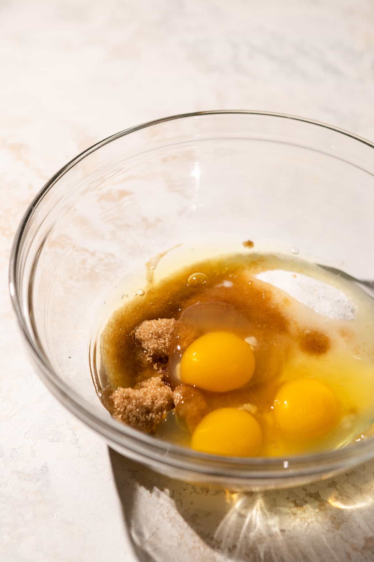 Eggs, sugar, brown sugar, vanilla, and almond extract in a glass bowl.