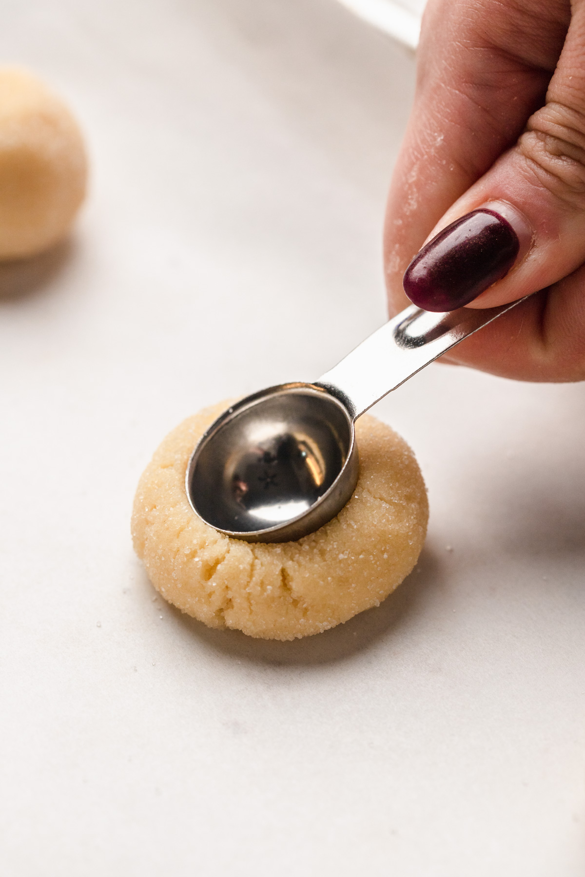 Pressing a teaspoon into a cookie dough ball.