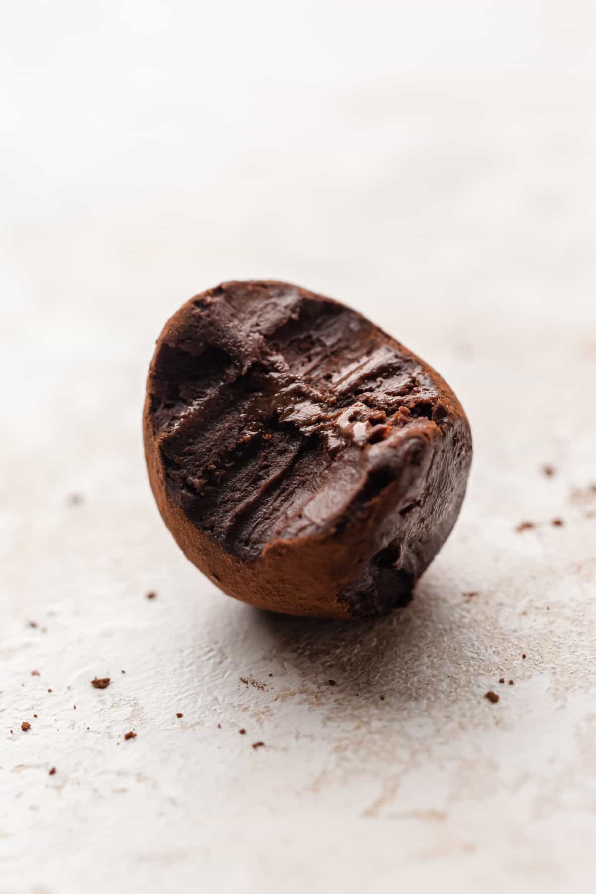 A close up of a chocolate truffle with a bite taken out of it.