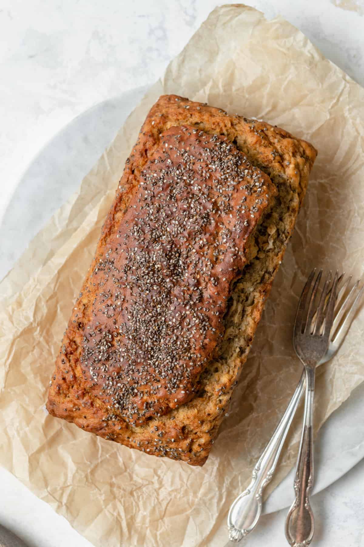 A loaf of banana bread topped with chia seeds on a piece of parchment paper.