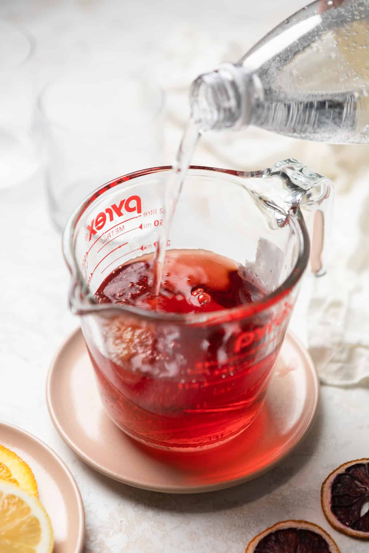 Pouring lemon sparkling water into red wine in a pitcher.