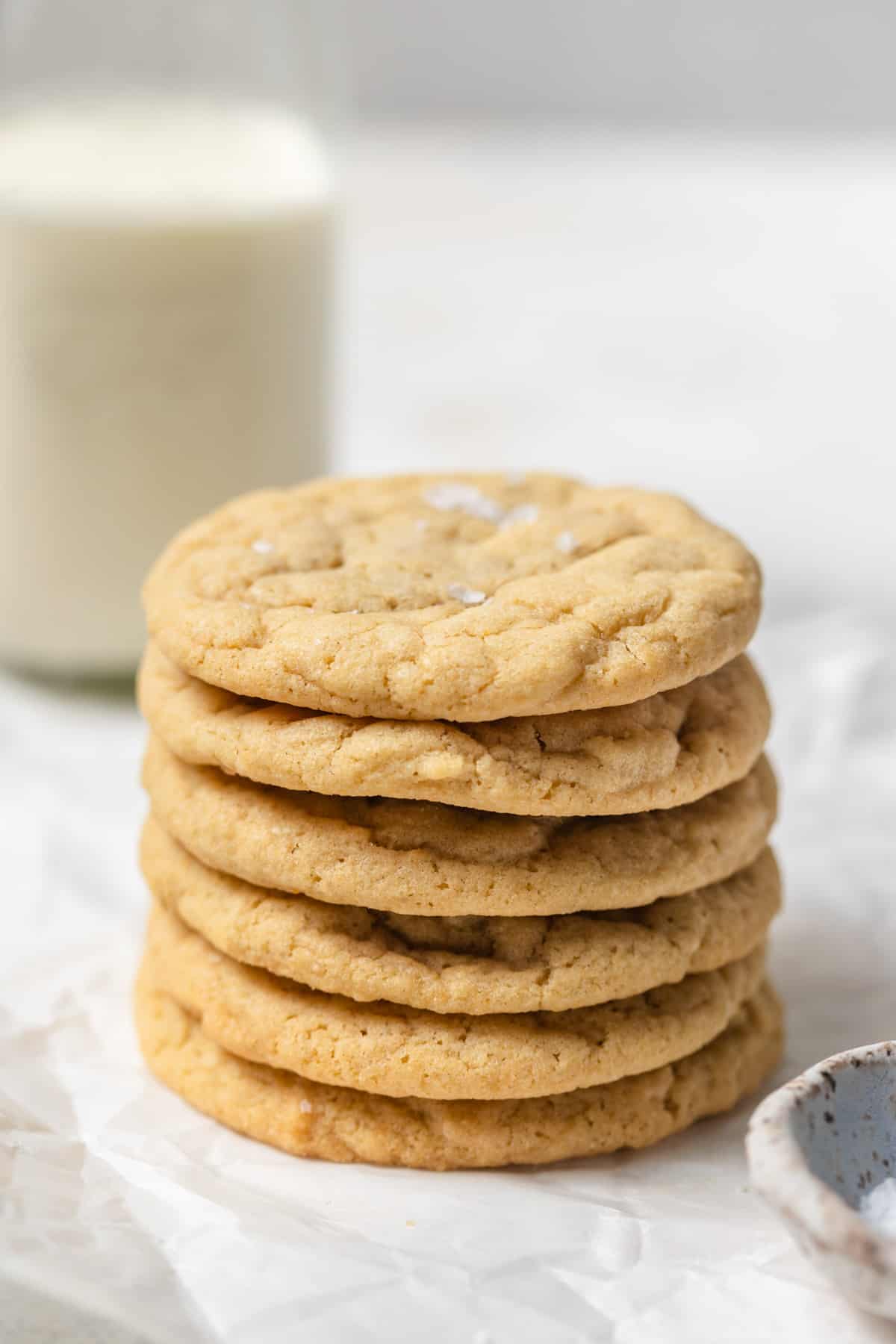 A stack of cookies on parchment paper with a glass of milk in the background.