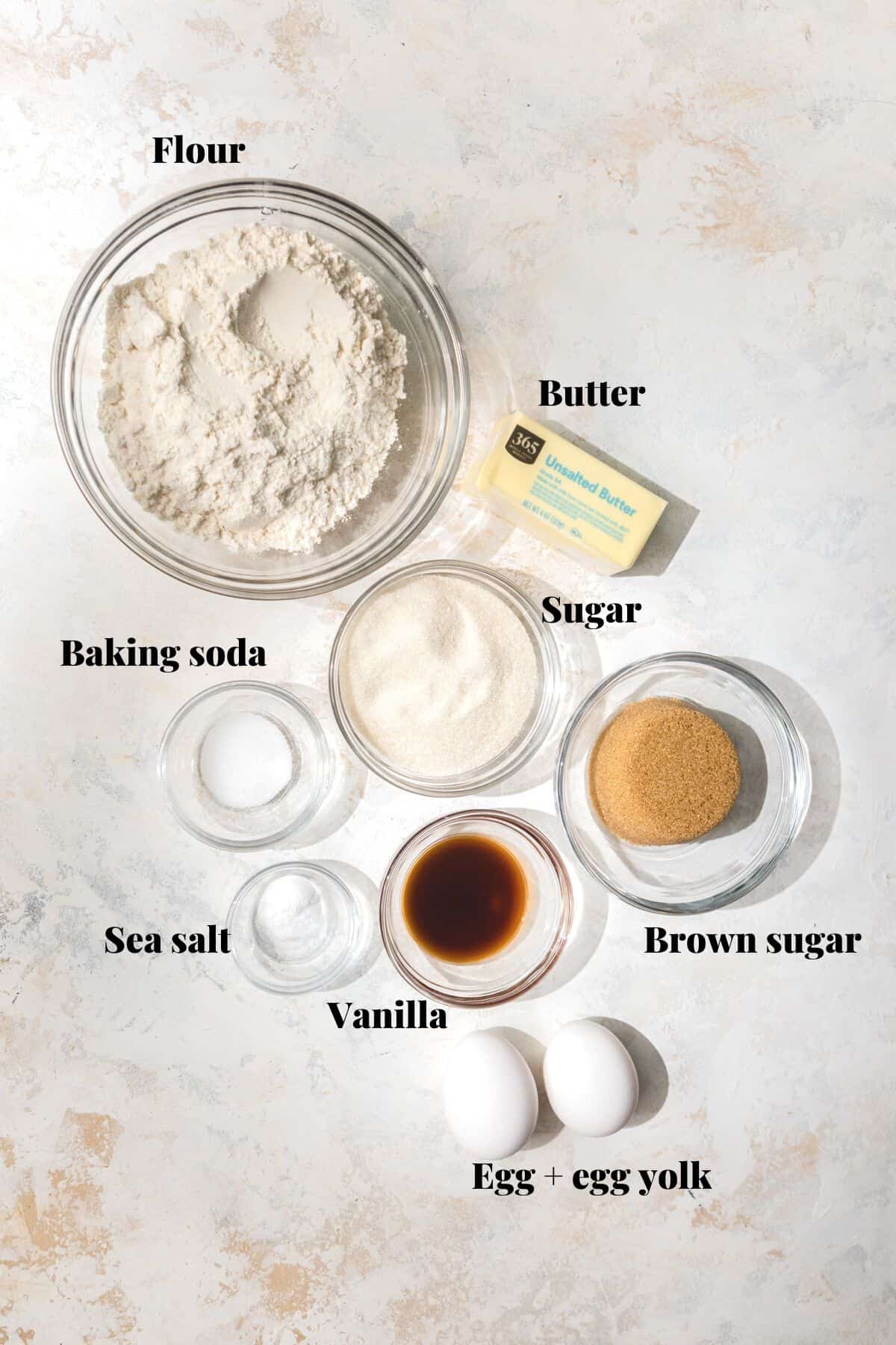 Ingredients to make cookies on a pink and white surface.