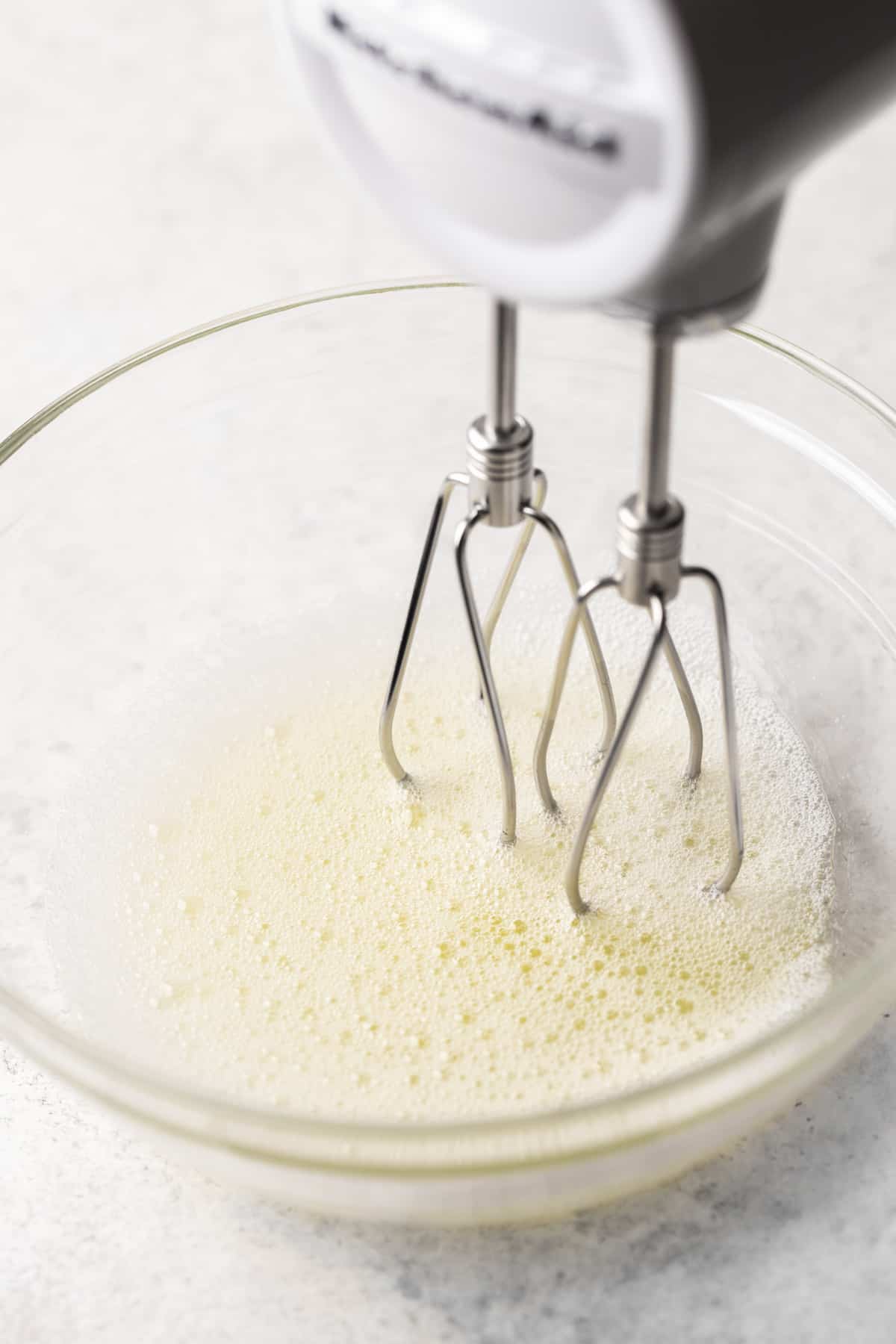 Frothy egg whites being mixed with a hand mixer.