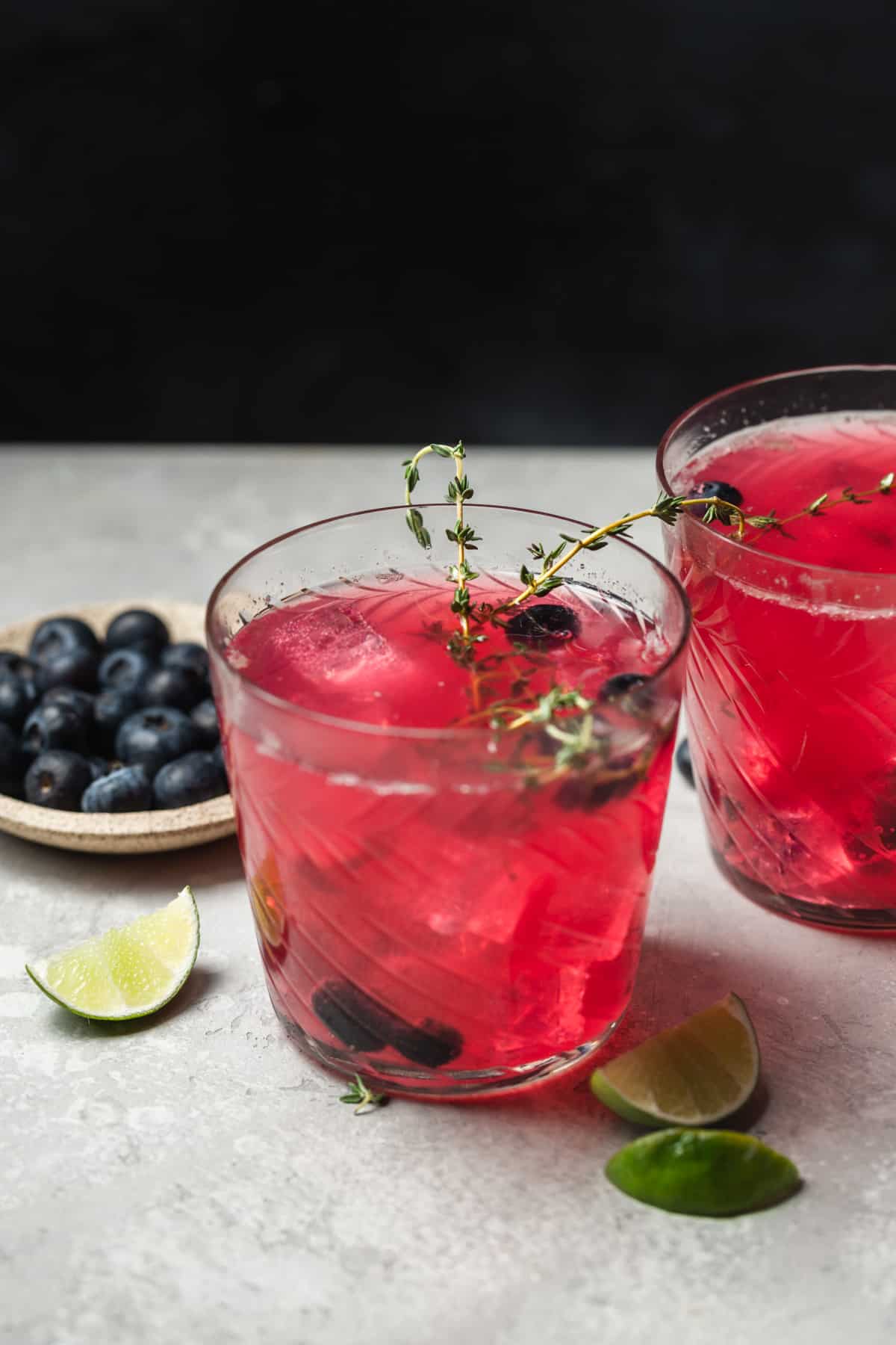 A blueberry gin and tonic cocktail in a glass garnished with blueberries and thyme.