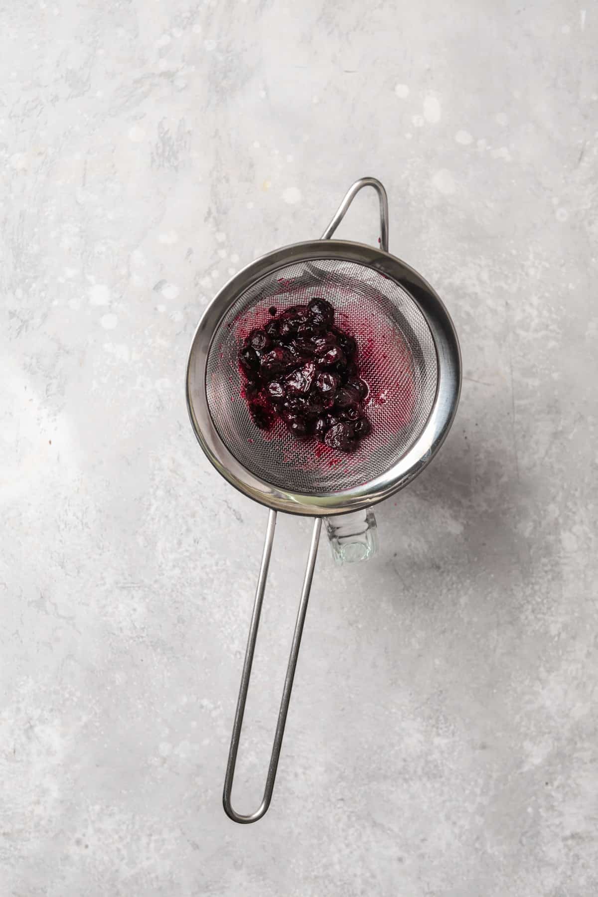 Blueberries in a sifter over a measuring cup.