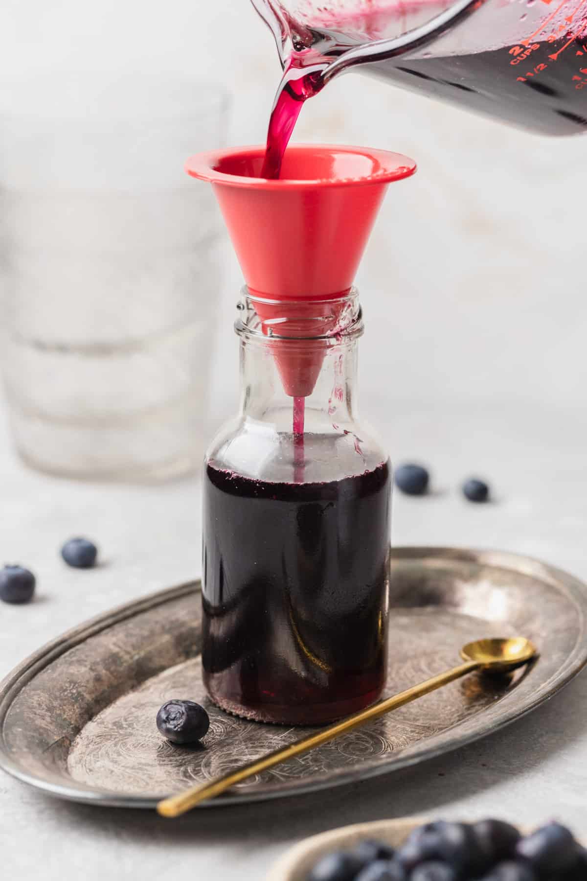 Blueberry syrup being poured through a funnel into a jar.