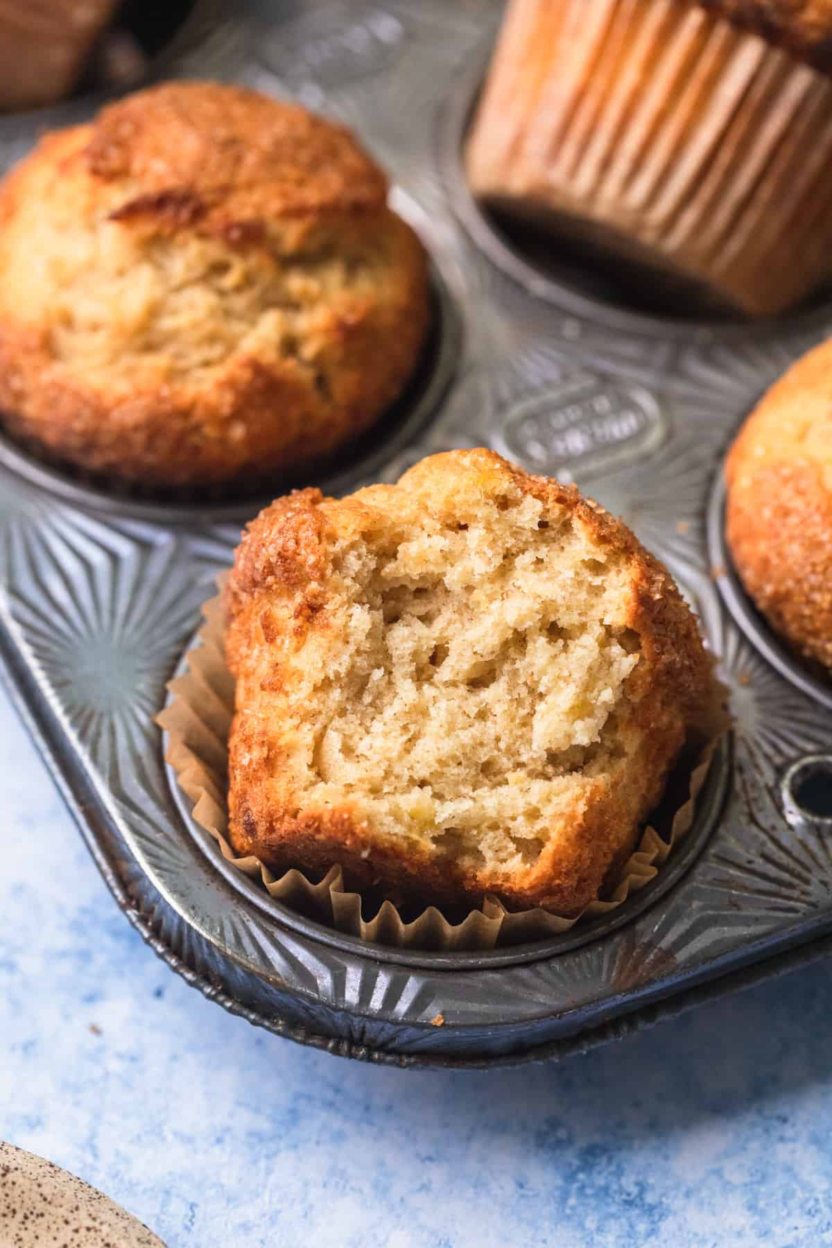 A muffin in a muffin tin with a bite taken out of it.