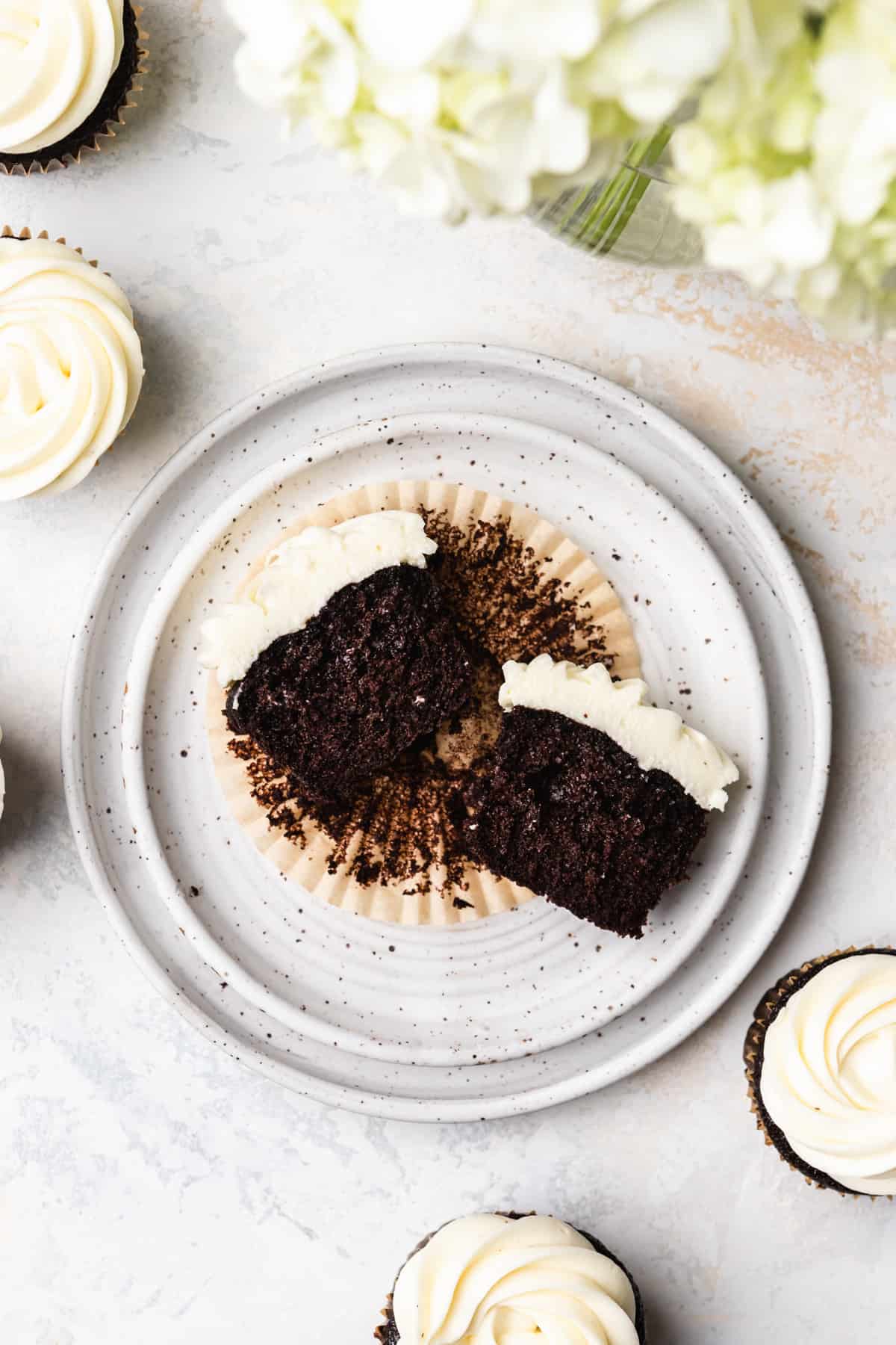 A chocolate cupcake with cream cheese frosting cut in half on a white plate.