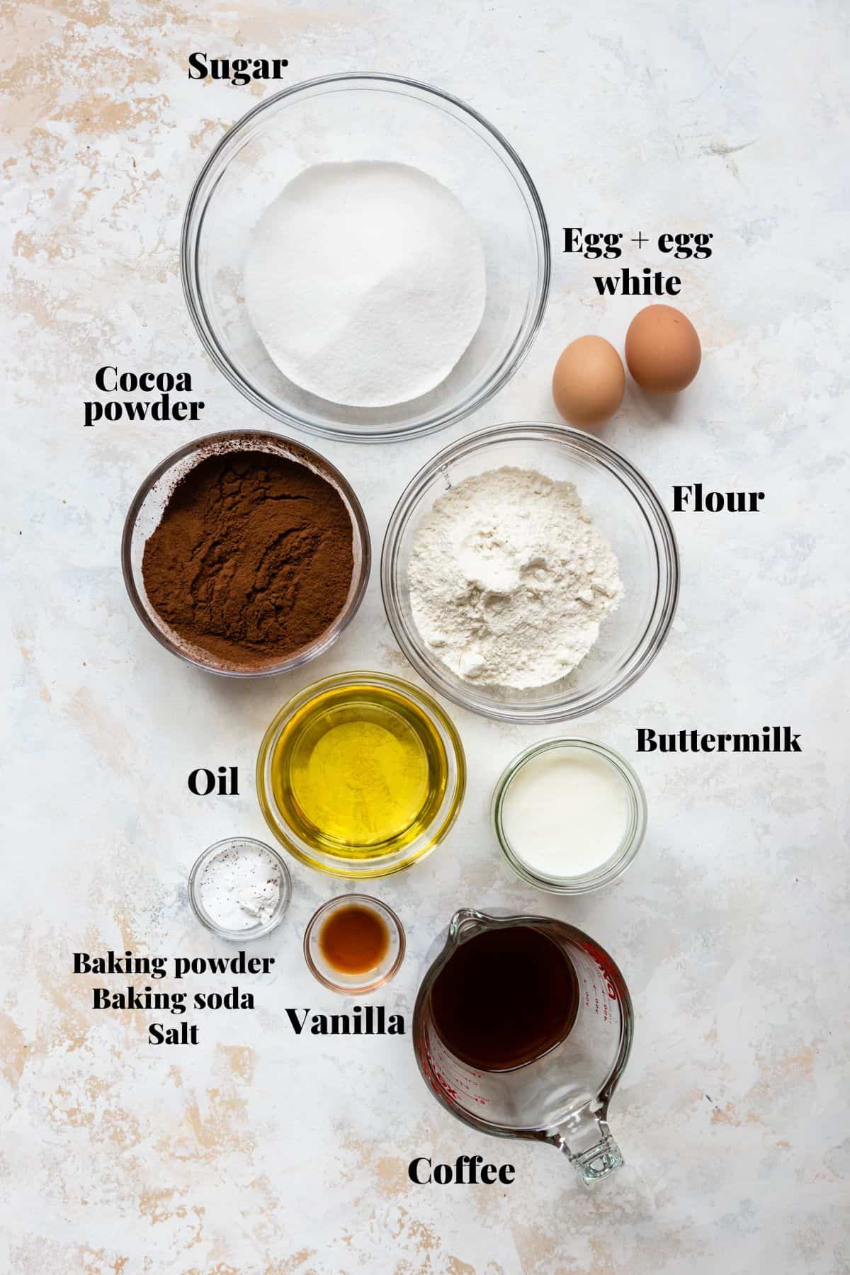 Ingredients to make chocolate cupcakes on a white and pink surface.