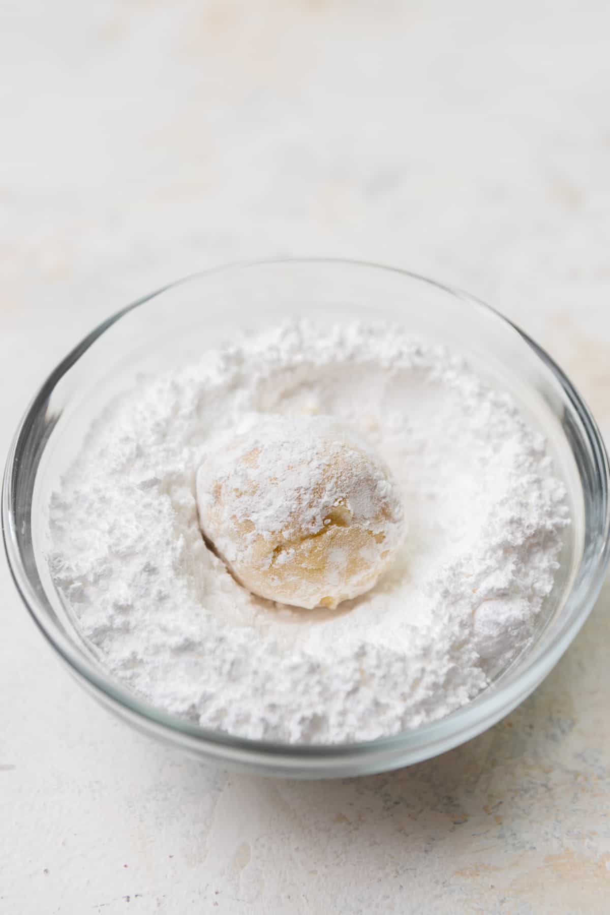 A cookie dough ball in a bowl of powdered sugar.