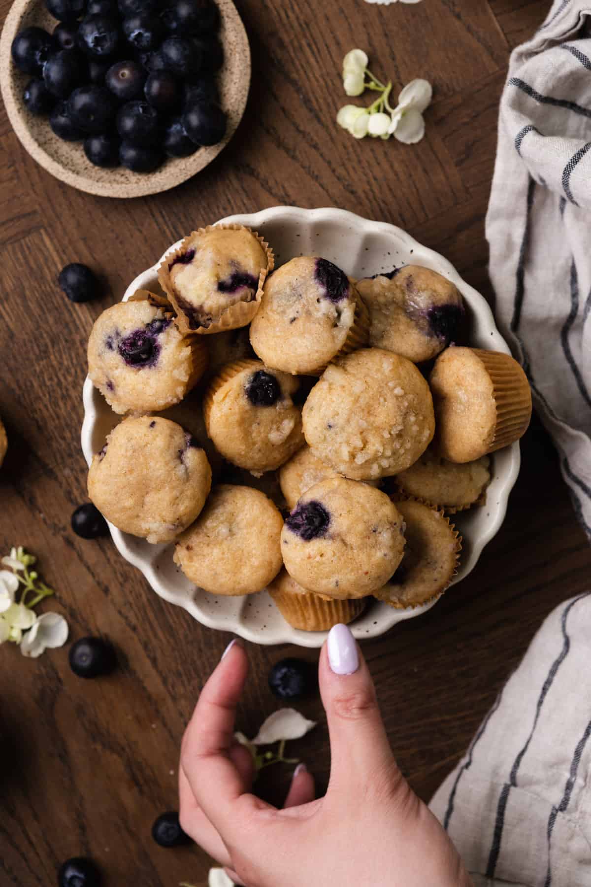 A bowl of mini blueberry muffins with a hand reaching for one.