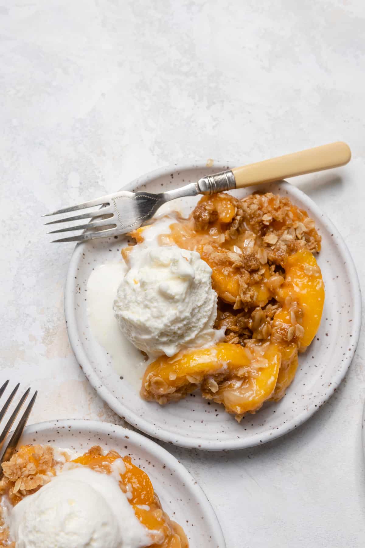 Peach crisp with ice cream on a white plate.