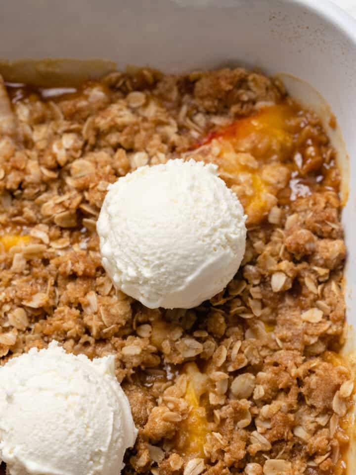 Peach crisp with a scoop of vanilla ice cream in a pan.