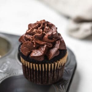A chocolate cupcake on a cupcake pan on a white surface.