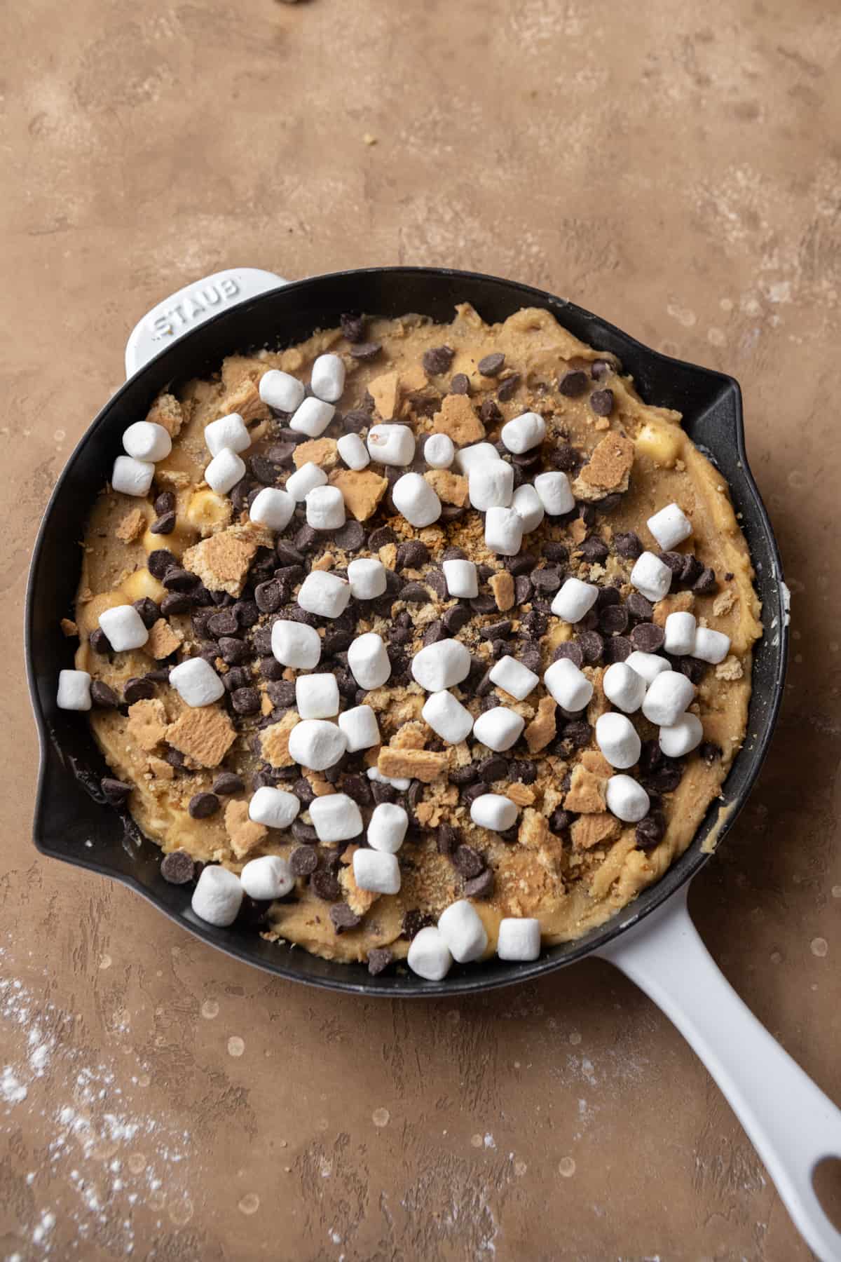 Cookie dough topped with marshmallows and graham crackers in a skillet.