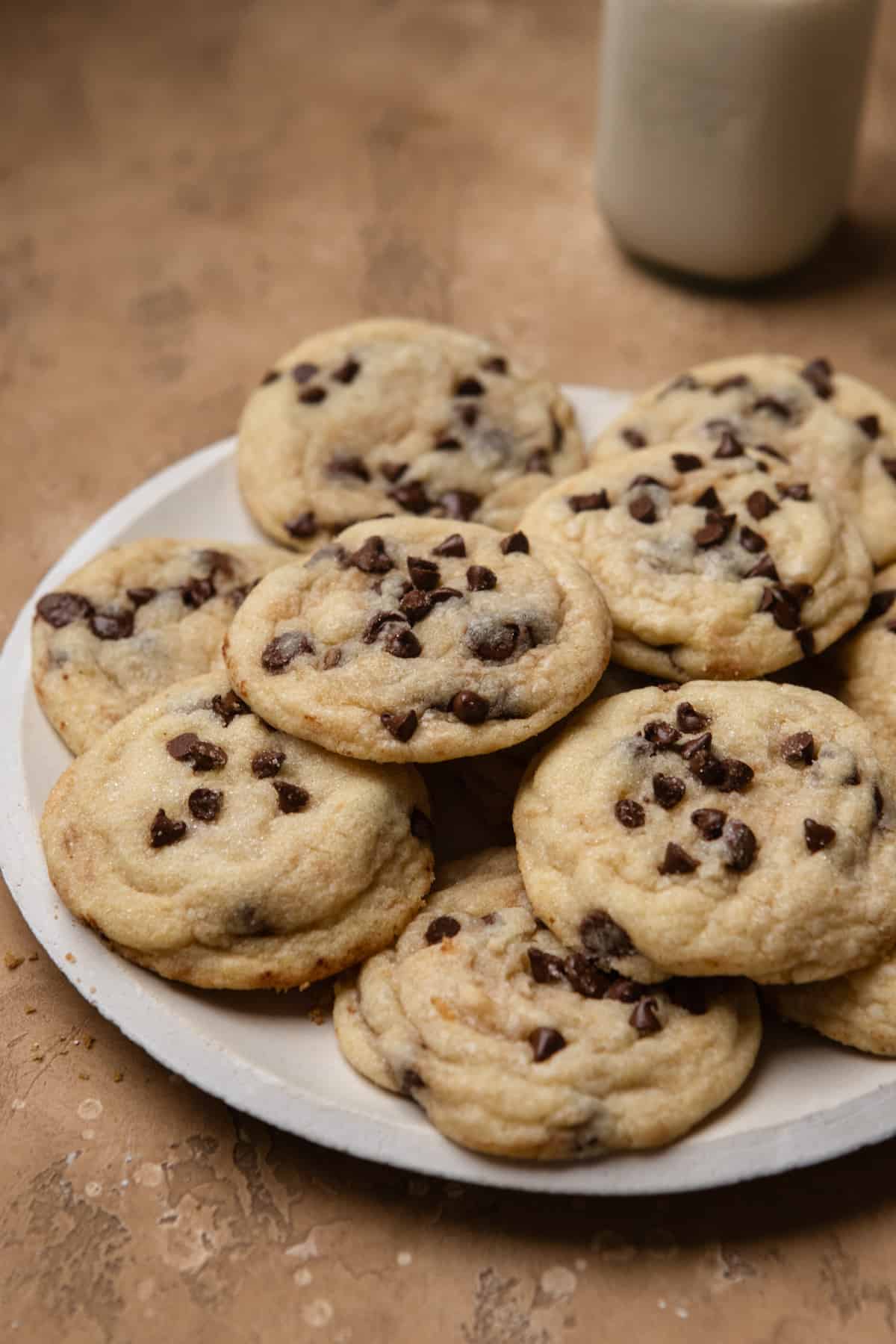 Chocolate chip cookies on a white plate with a bottle of milk in the background.