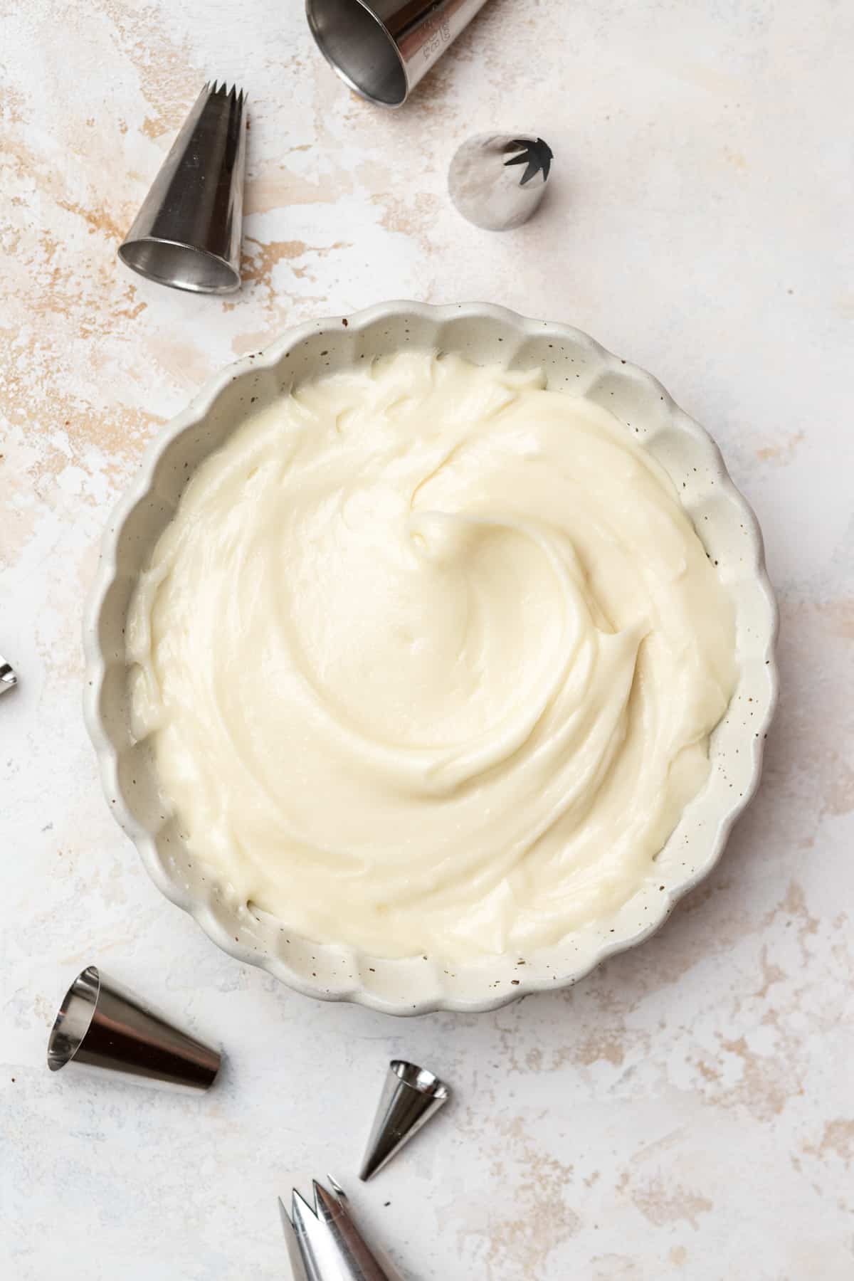 Cream cheese frosting in a bowl with piping tips around it.