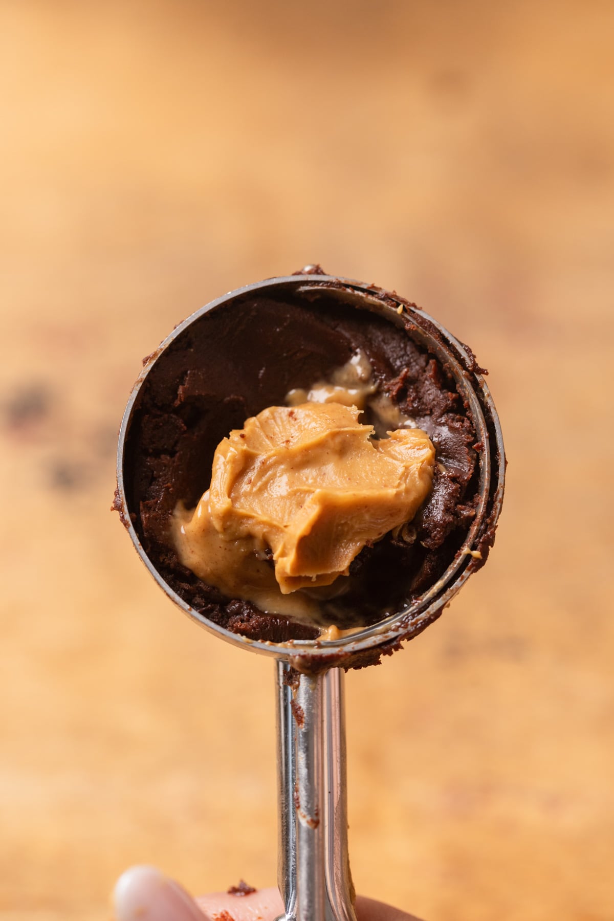 A cookie scoop with chocolate cookie dough and peanut butter in it.