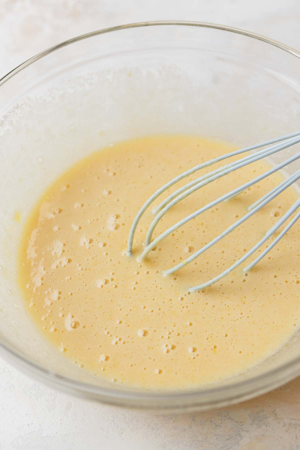 Eggs and sugar whisked together in a glass bowl.